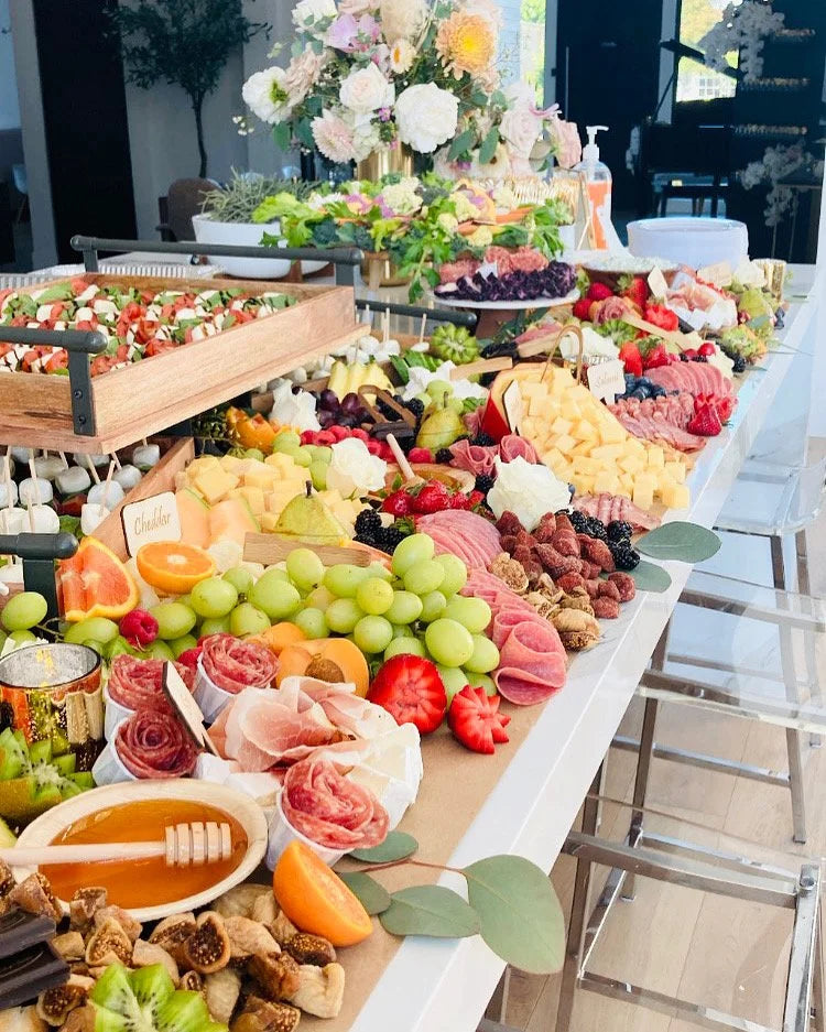 Gourmet food platter with fruits, meats, and cheeses on a table outdoors.