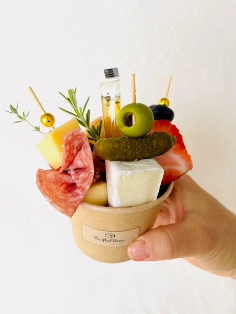 Hand holding a small cup with skewered food items on a white background