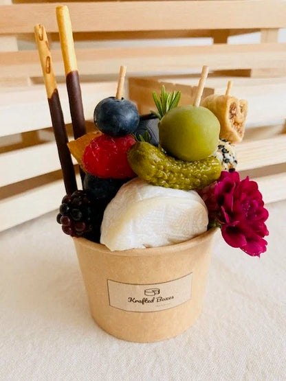 Festive arrangement of fruits and a flower in a paper cup with skewers on a wooden surface.