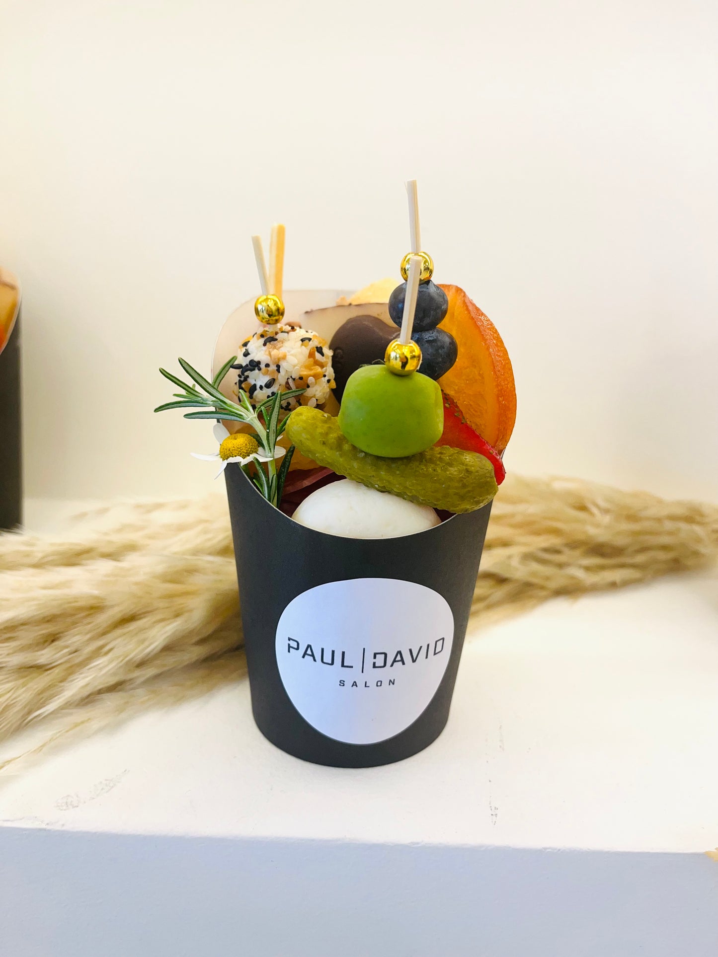 Decorative item with fruits and flowers in a black container labeled 'Pauli David' on a light background.