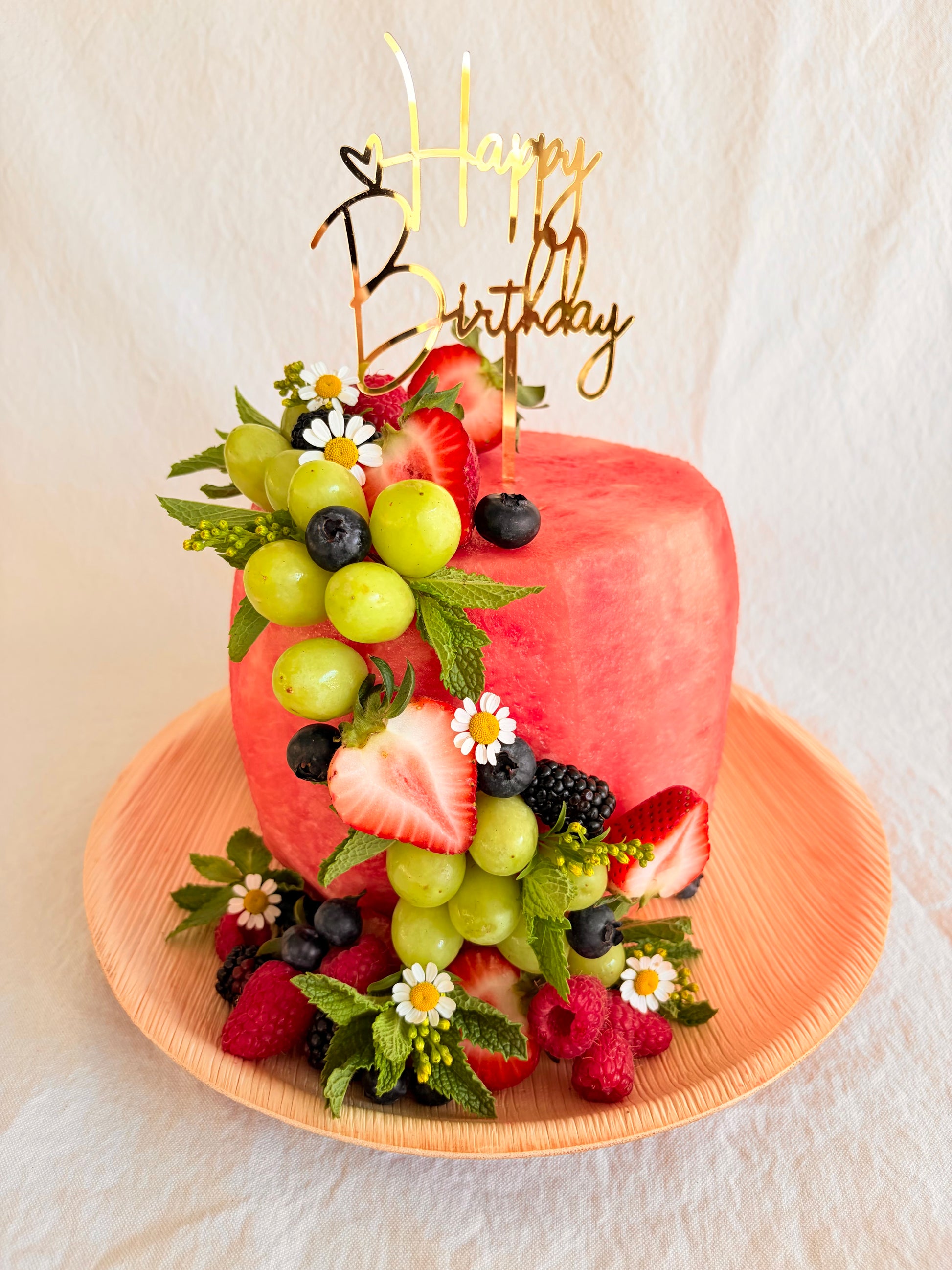 Fruit-themed birthday cake with 'Happy Birthday' topper on a white background