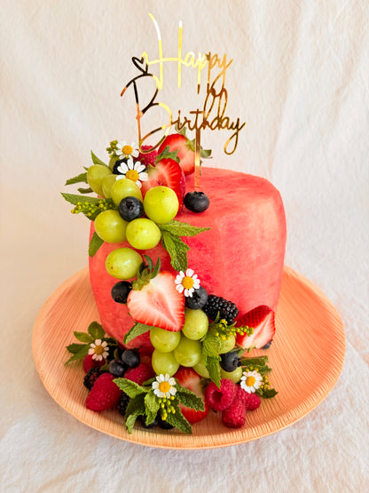 Fruit-themed birthday cake with 'Happy Birthday' topper on a white background