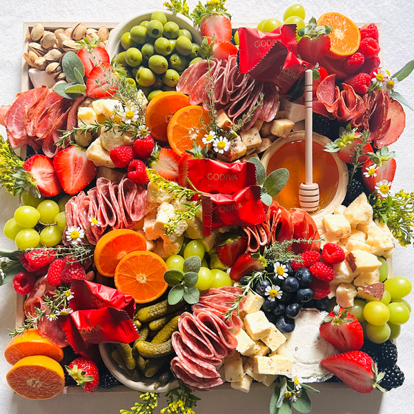 Gourmet charcuterie board with meats, cheeses, fruits, and vegetables on a white surface.