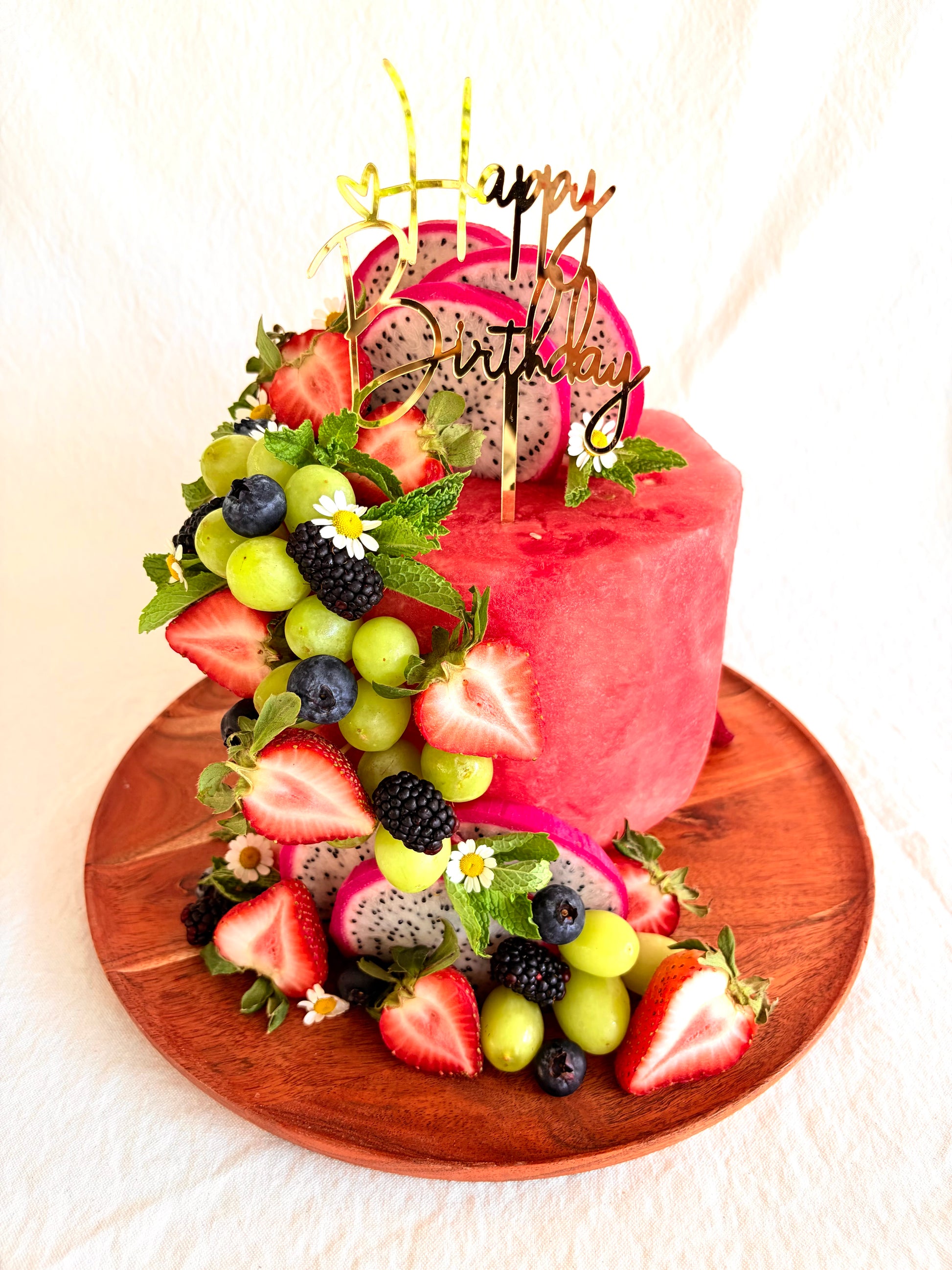 Fruit-themed birthday cake with colorful fruits and a 'Happy Birthday' topper on a wooden board.