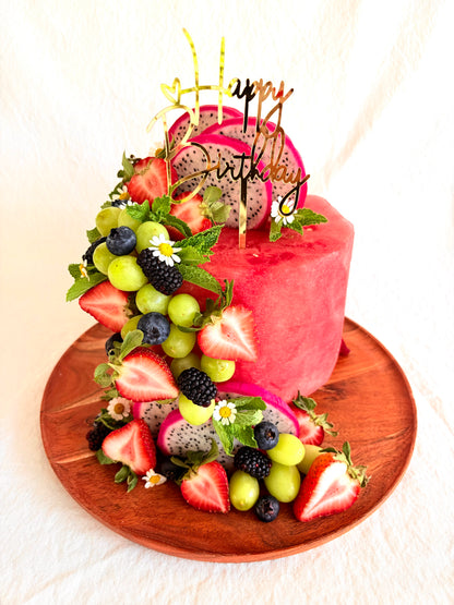 Fruit-themed birthday cake with colorful fruits and a 'Happy Birthday' topper on a wooden board.