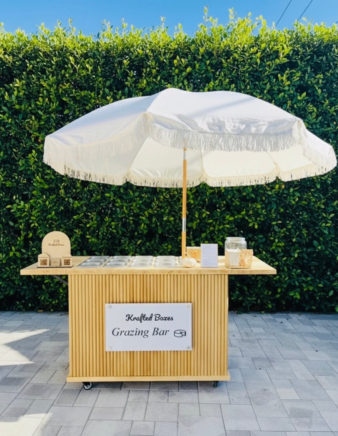 Grazing bar with a large white umbrella against a green hedge.